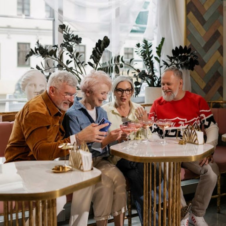 Four senior adults chatting and laughing together in a cozy café setting.