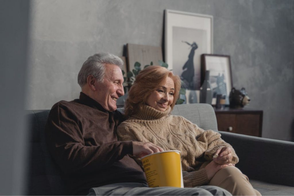 A couple sitting on a sofa with a pack of popcorn.