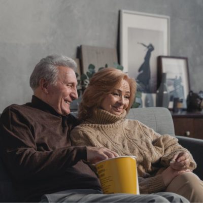 A couple sitting on a sofa with a pack of popcorn.