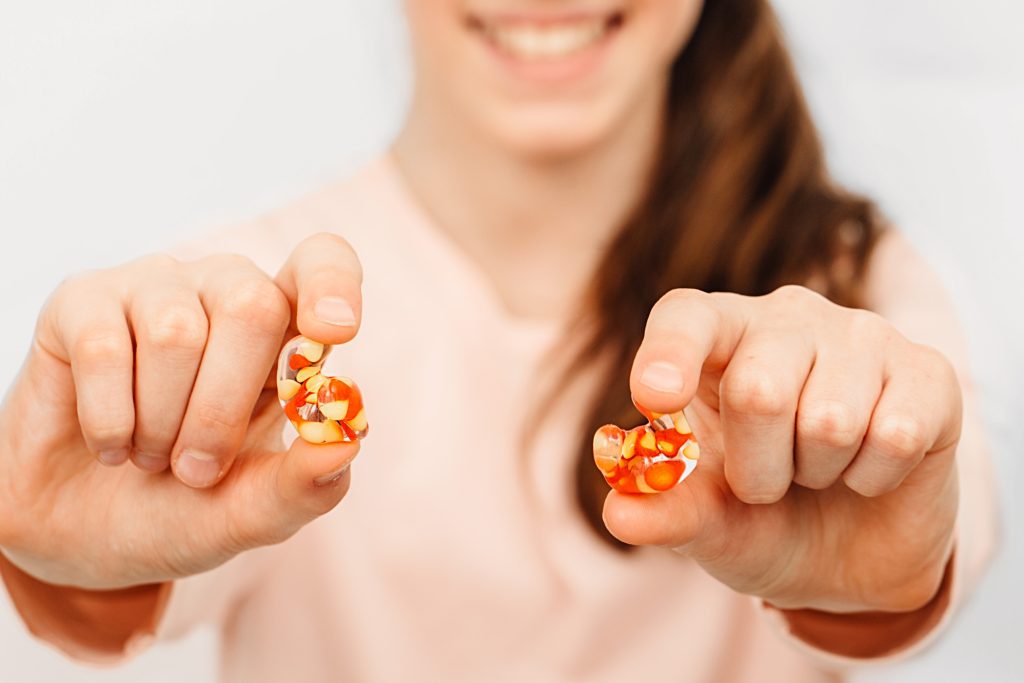 A close-up view of custom-molded earplugs being held by a young girl, with a blurred background focusing attention on the earplugs.