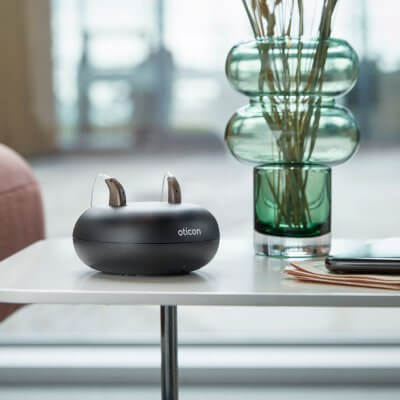 A pair of hearing aids Oticon More in a charging doc.