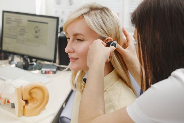 An audiologist examining a patient's ear using an otoscope during a hearing check-up.