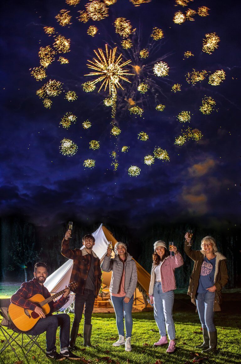 A group of friend in front of a tent watching fireworks.