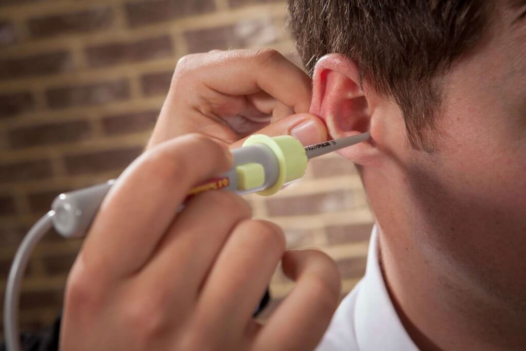 An audiologist performing water irrigation on a patient for ear wax removal.