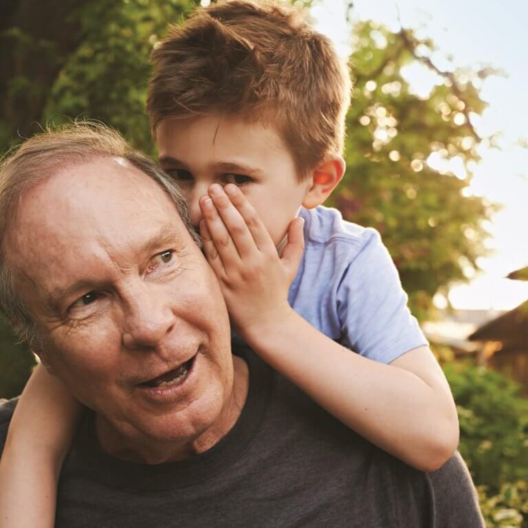 A child whispering in to grandads ears.