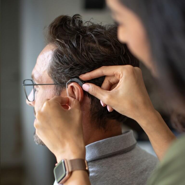 Close up shot of a hearing aid dispenser fitting hearing aids.