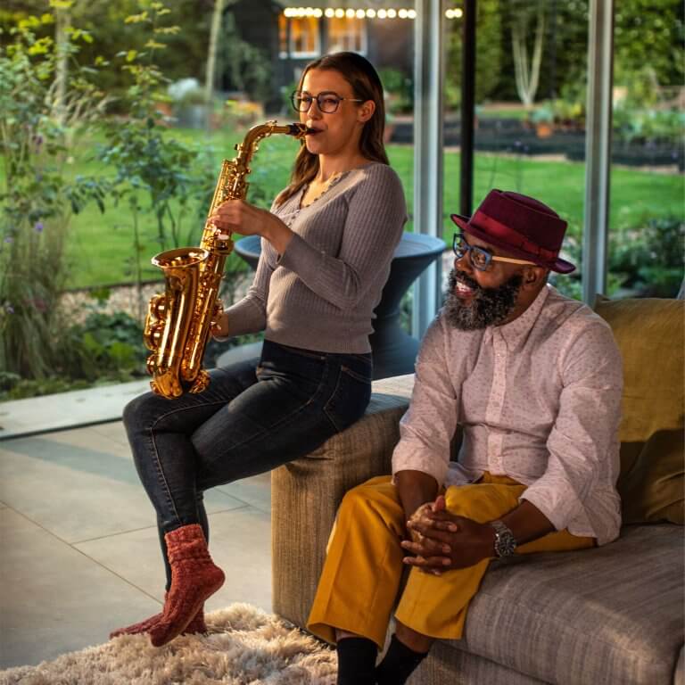 Girl playing saxaphone sat on the edge of a sofa