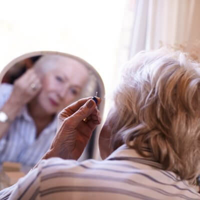 An elderly woman putting her hearing aid on.