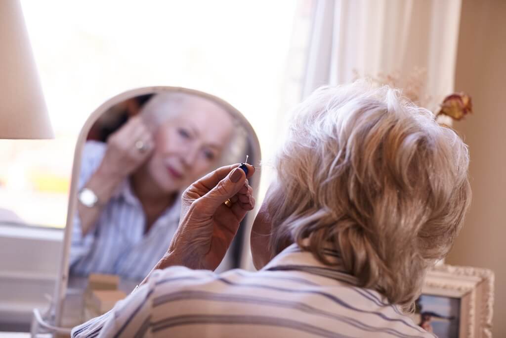 An elderly woman putting her hearing aid on.