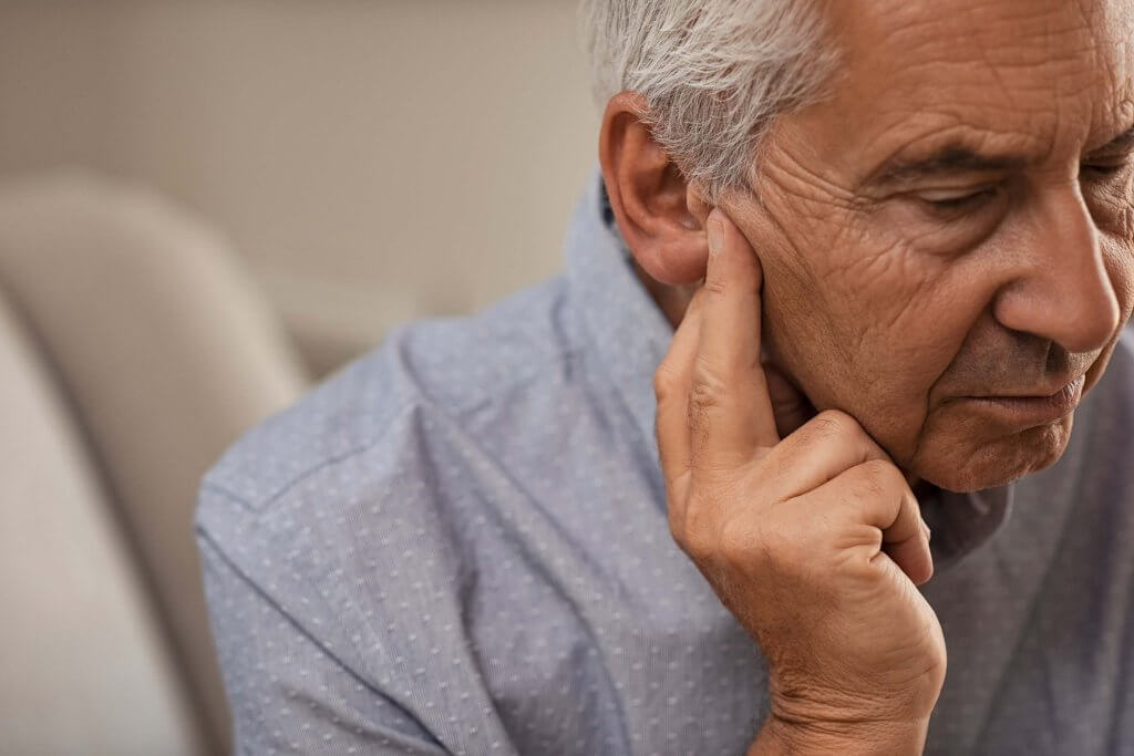 An old man holding his ear and appearing to be in pain.