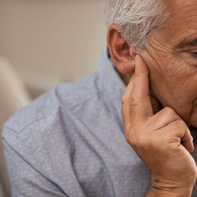 An old man holding his ear and appearing to be in pain.