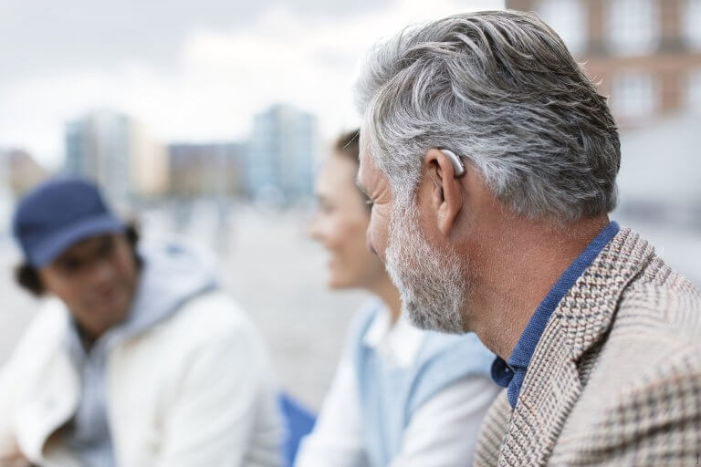 A man wearing a hearing aid talking to people outside.