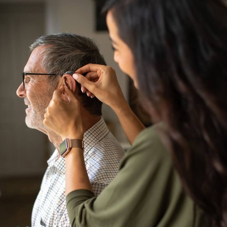 Side view of an audiologist fitting a hearing aid in a patient's ear.