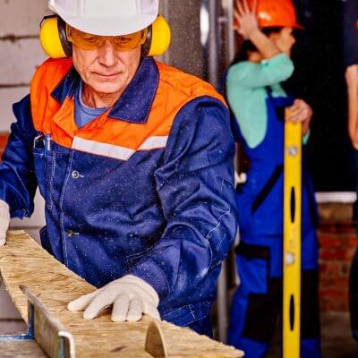 A man working with wood while wearing ear defenders.