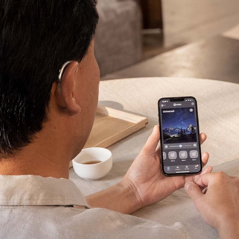 A man wearing a hearing aid and using Widex app on his phone.