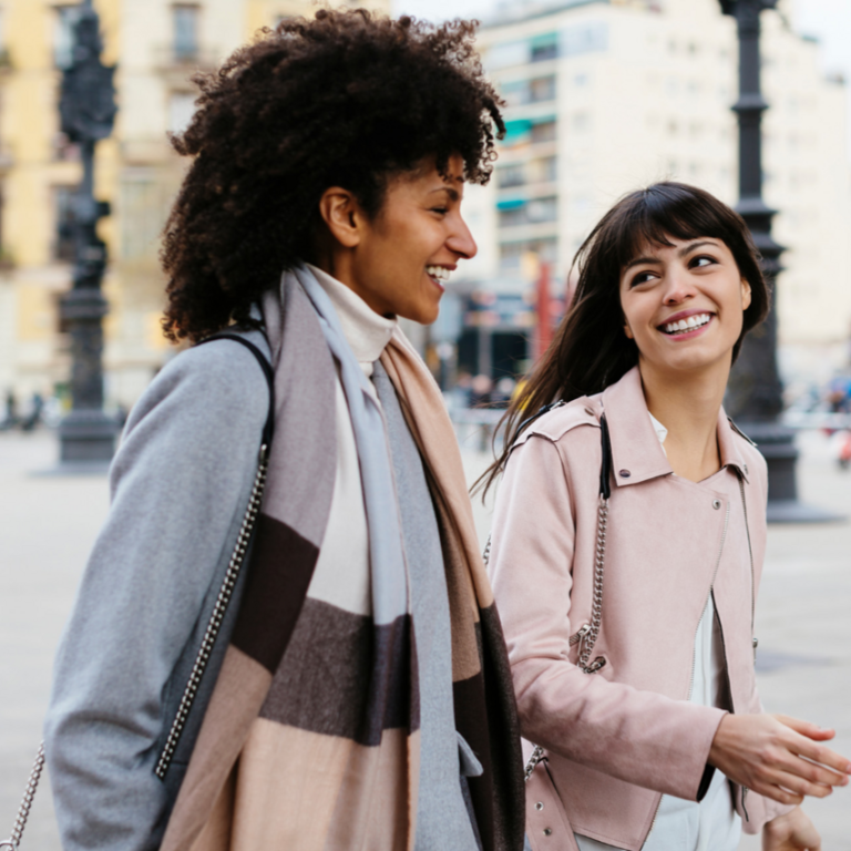 Two women walking in the street and smiling.