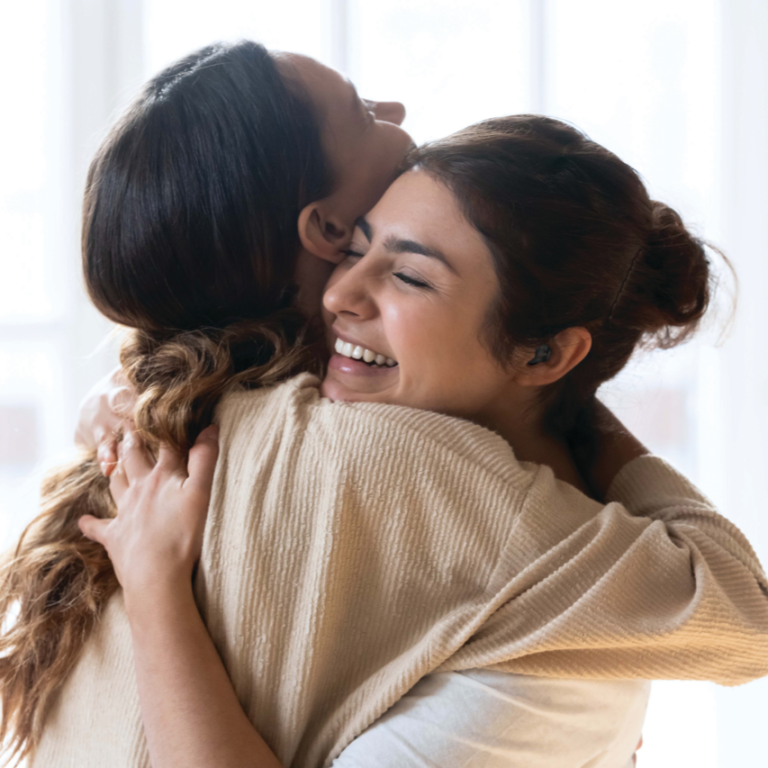 Two women hugging with one with hearing aids.