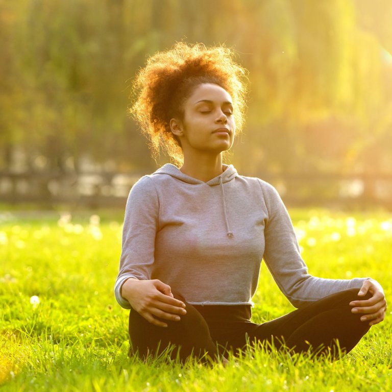 A woman sitting on the grass and doing meditation.