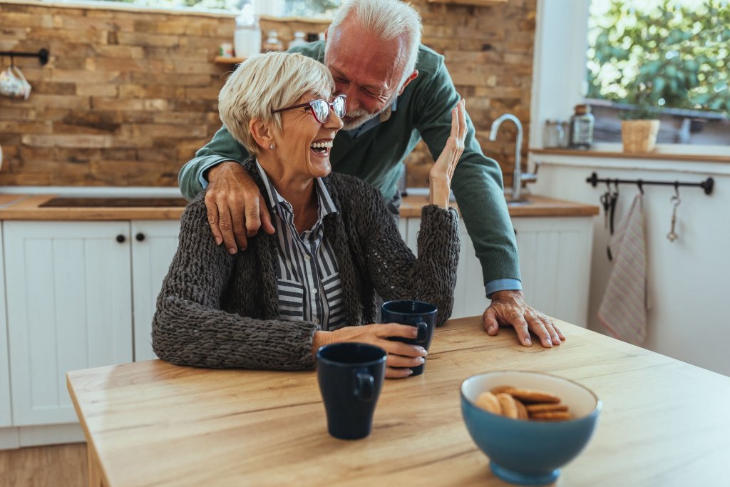 A man whispering into his wife's ear while she laughs.