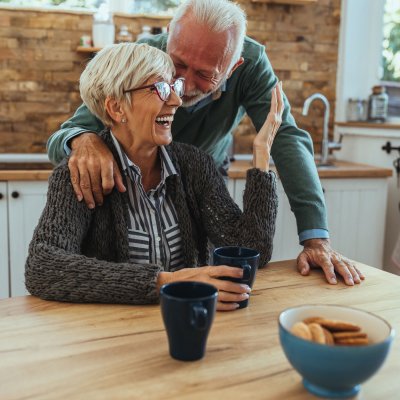 A man whispering into his wife's ear while she laughs.