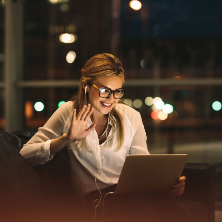 A woman with glasses waving during her video call on her tablet.