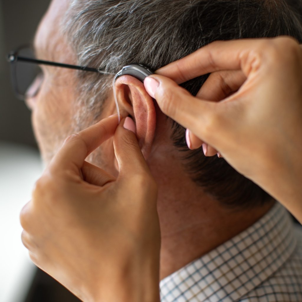 An audiologist fitting a hearing aid in a man's ear.