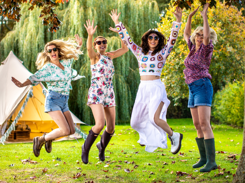 Four women jumping in the air in front of a tent.