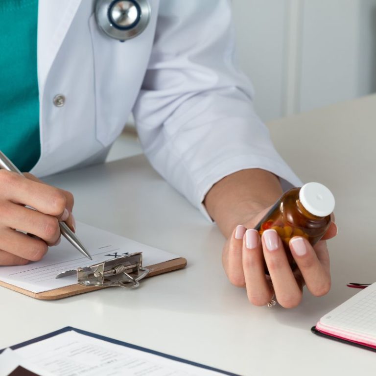 Close-up view of a female doctor’s hand holding a bottle of pills while writing a prescription.