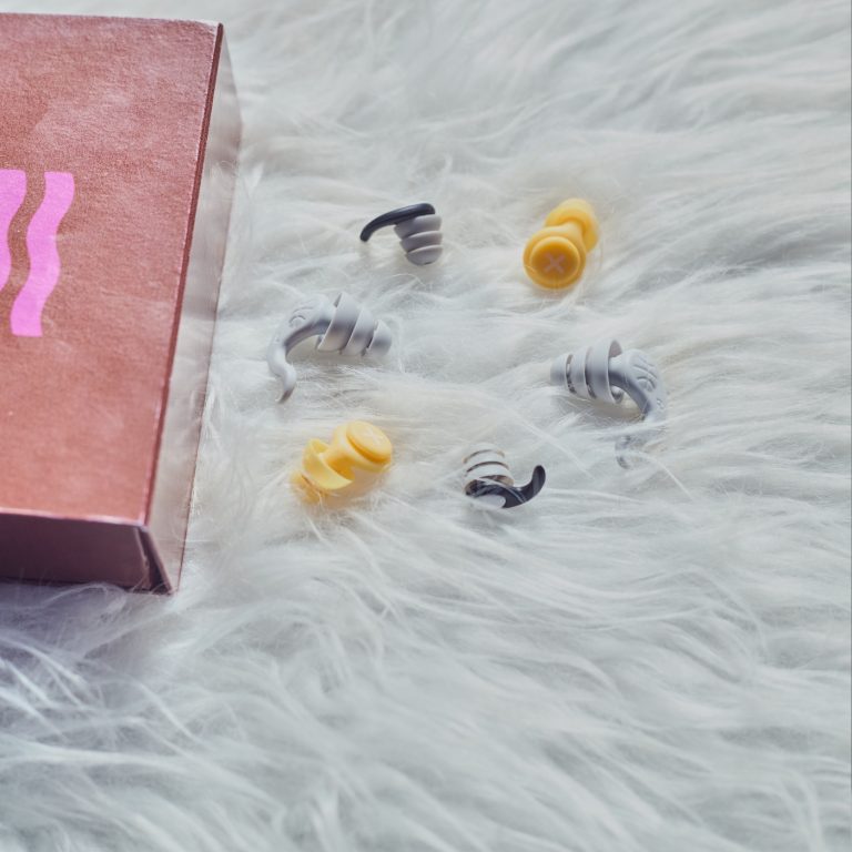 Colorful earplugs spill from a box onto a fluffy white surface.