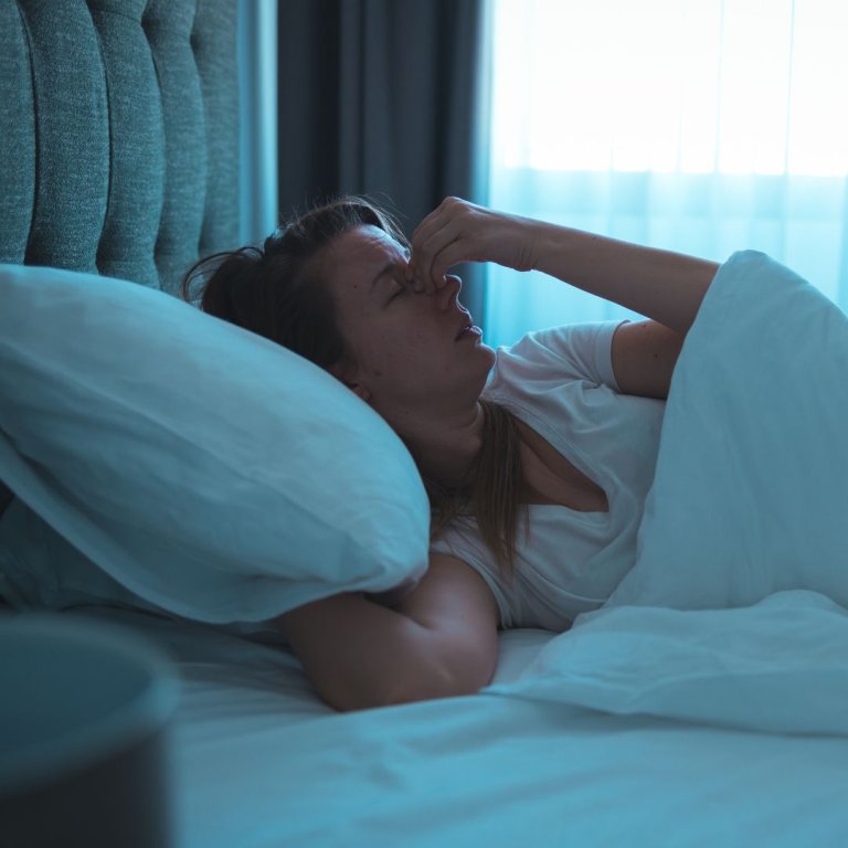 A woman appearing to struggle to fall asleep on her bed.