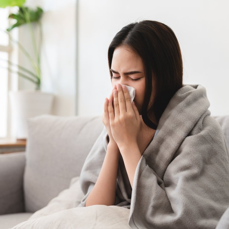 A young woman wearing a blanket on her back and blowing her nose.