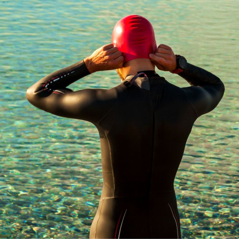 A man wearing a wetsuit and putting on a swim cap.