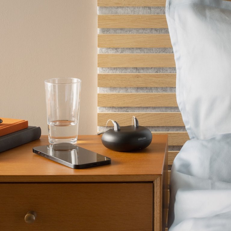 Oticon Real in charger square on a bedside table.