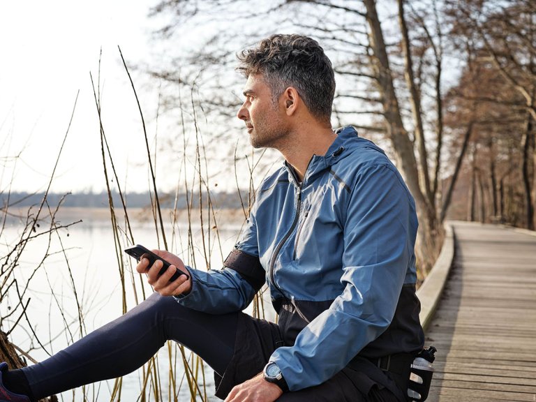 A runner wearing hearing aids, stretching, and holding his phone.