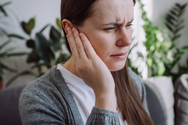 A woman appears to be in pain, touching her ear.