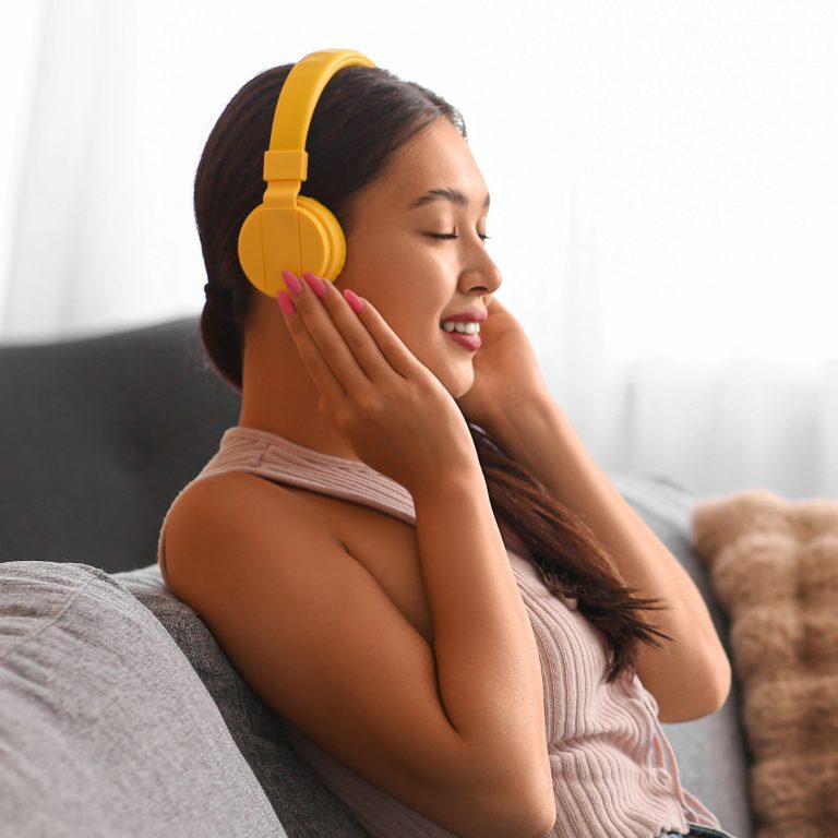 Happy Asian woman in headphones listening music on sofa at home