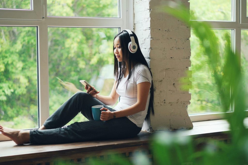 Woman relaxing with headphones by sunny window.