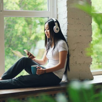 Woman relaxing with headphones by sunny window.