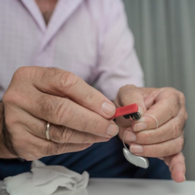 Man cleaning a hearing aid with a brush.