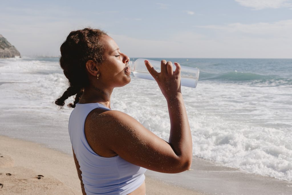 Woman driking water from a bottle by the beach.