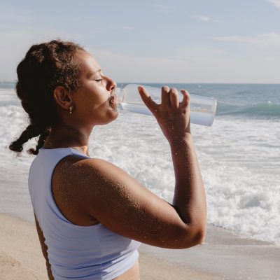 Woman driking water from a bottle by the beach.