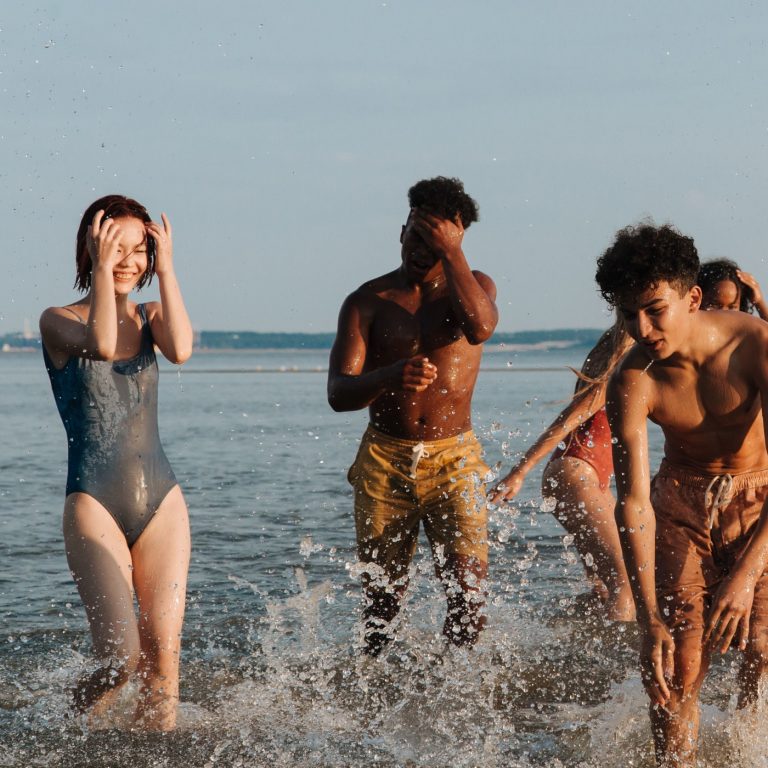 Group of teenagers playing and splashing in the sea, embracing a joyful summer day by the beach.
