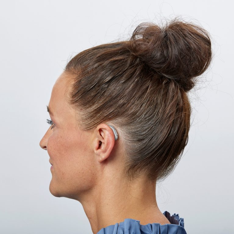 Woman wearing Oticon Reveal behind her ear with receiver in canal.