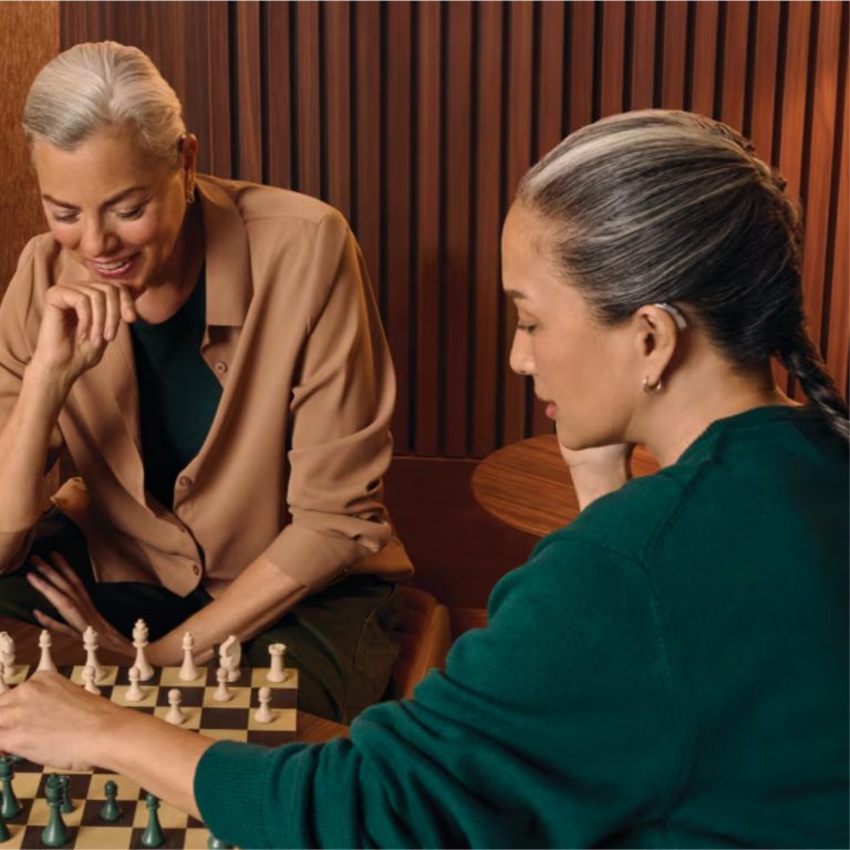 Two woman playing chess with one wearing a hearing aid.